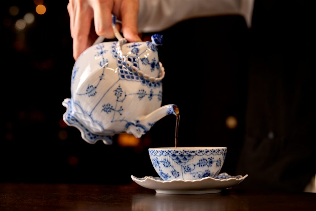 青い花模様のポットから紅茶を注ぐ